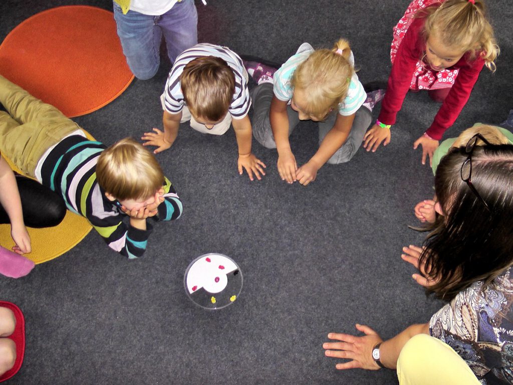 Kinder knien und liegen im Kreis um ein rundes Spielgerät