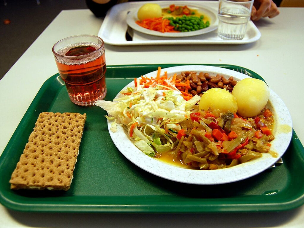 ein grünes Kantinentablett mit einem Stück Knäckebrot, einem Getränk und einem Teller mit Gemüse und Kartoffeln